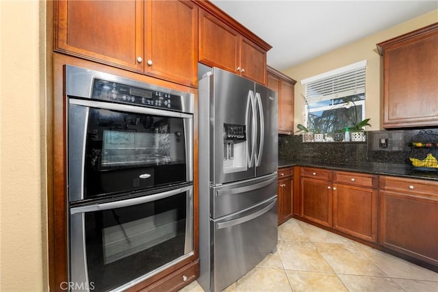 kitchen with tasteful backsplash, light tile patterned floors, dark stone counters, and appliances with stainless steel finishes