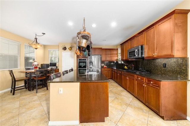 kitchen with hanging light fixtures, tasteful backsplash, dark stone countertops, an island with sink, and appliances with stainless steel finishes