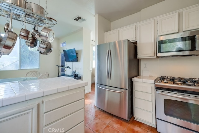 kitchen with appliances with stainless steel finishes, light tile patterned flooring, tile countertops, and white cabinetry