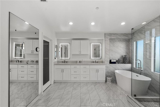 full bathroom featuring double vanity, marble finish floor, a freestanding bath, and recessed lighting