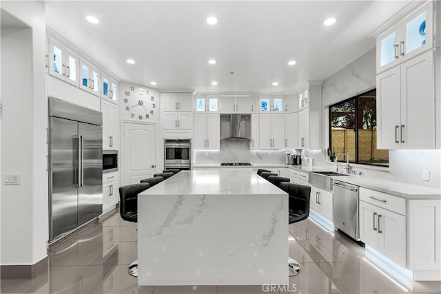 kitchen with white cabinetry, a kitchen island, built in appliances, and wall chimney exhaust hood