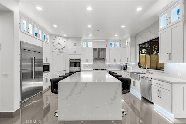 kitchen featuring wall chimney exhaust hood, a center island, glass insert cabinets, and built in appliances