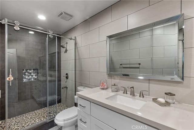 bathroom featuring a shower with shower door, tile walls, decorative backsplash, vanity, and toilet