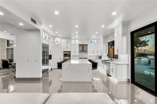 kitchen with glass insert cabinets, white cabinetry, wall chimney range hood, and built in appliances