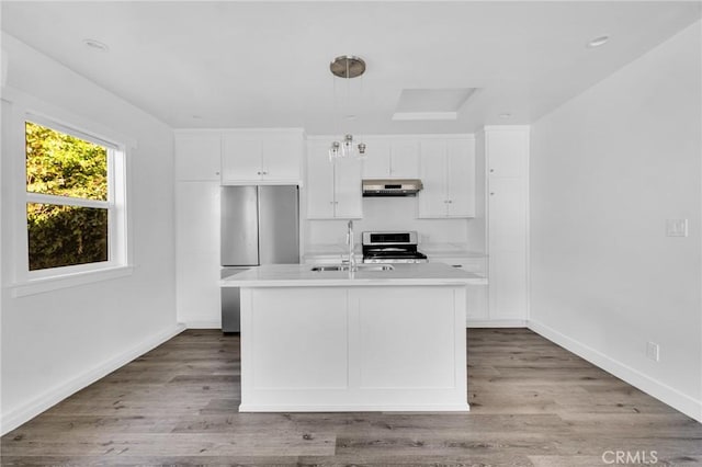 kitchen featuring a center island with sink, white cabinets, range, and stainless steel refrigerator