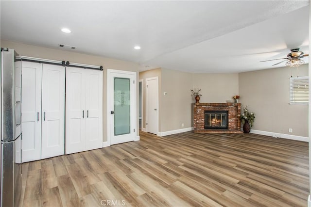 unfurnished living room with a fireplace, ceiling fan, and light hardwood / wood-style flooring