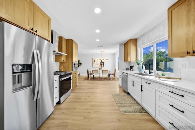 kitchen featuring sink, light wood-type flooring, stainless steel appliances, white cabinets, and wall chimney exhaust hood