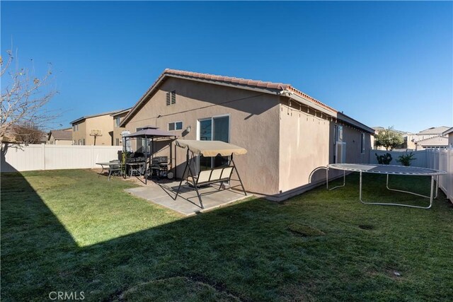 rear view of house with a yard, a trampoline, and a patio area