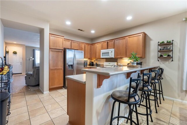 kitchen with white appliances, a kitchen breakfast bar, kitchen peninsula, and light tile patterned flooring