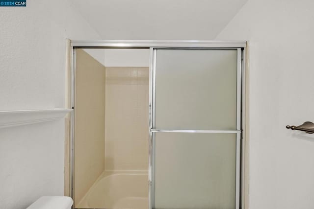 bathroom featuring a shower with door and toilet