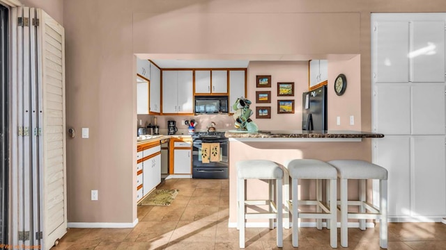 kitchen featuring a breakfast bar area, light tile patterned flooring, white cabinets, and black appliances