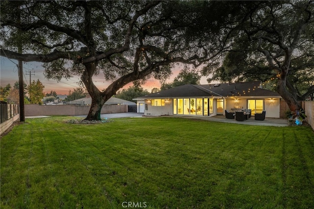 back house at dusk featuring a yard, an outdoor hangout area, and a patio area