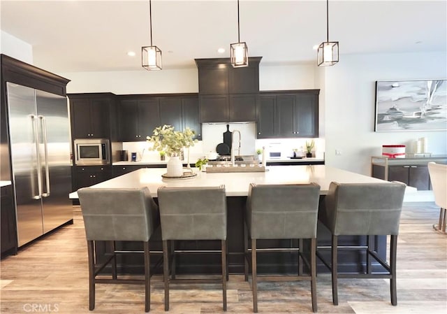 kitchen with a large island, hanging light fixtures, built in appliances, light hardwood / wood-style floors, and a breakfast bar area