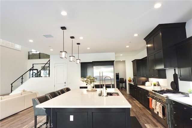 kitchen with hanging light fixtures, dark hardwood / wood-style floors, a large island with sink, a breakfast bar area, and high quality appliances