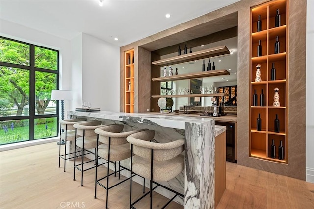 bar featuring light stone counters, beverage cooler, and light wood-type flooring