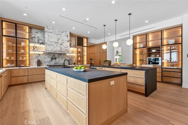 kitchen featuring sink, light wood-type flooring, a kitchen island with sink, and hanging light fixtures