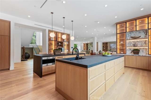 kitchen featuring sink, an island with sink, decorative light fixtures, and light wood-type flooring