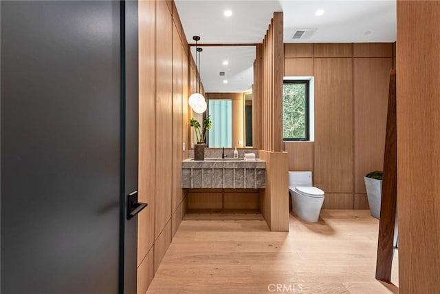 bathroom featuring vanity, toilet, wood-type flooring, and wooden walls