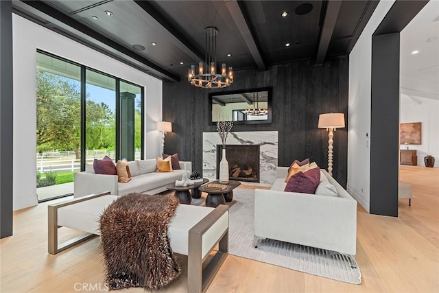 living room with beam ceiling, a high end fireplace, light hardwood / wood-style floors, and a notable chandelier