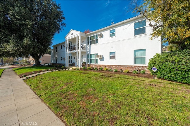 view of front of house featuring a balcony, an AC wall unit, and a front lawn