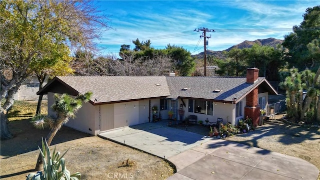 ranch-style house featuring roof with shingles, a chimney, stucco siding, concrete driveway, and a mountain view