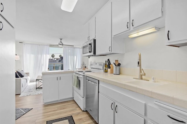 kitchen featuring white cabinetry, tile counters, ceiling fan, appliances with stainless steel finishes, and light wood-type flooring