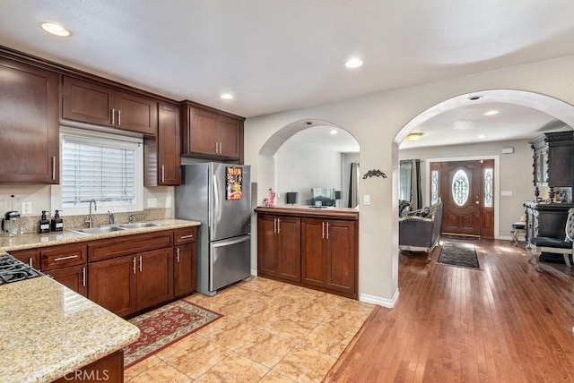 kitchen featuring stainless steel fridge, light stone counters, sink, and light hardwood / wood-style flooring