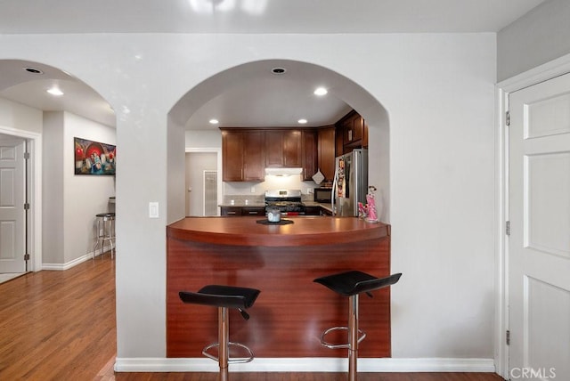 kitchen with appliances with stainless steel finishes, hardwood / wood-style flooring, and a kitchen breakfast bar