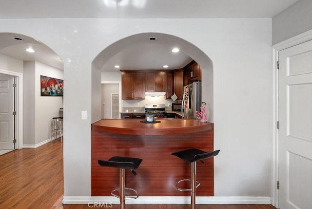 1417 W Gage Ave, Los Angeles, CA 90047 - kitchen featuring appliances with stainless steel finishes, a kitchen breakfast bar, arched walkways, wood finished floors, and recessed lighting