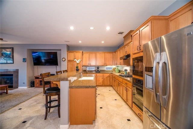 kitchen with sink, a kitchen breakfast bar, a tile fireplace, a kitchen island with sink, and black appliances