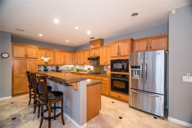 kitchen with a kitchen island with sink, black appliances, and a kitchen bar