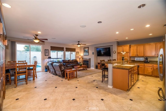 kitchen with ceiling fan, sink, a kitchen bar, a tiled fireplace, and a center island with sink