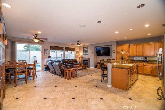 kitchen with sink, stainless steel fridge, a kitchen bar, ceiling fan, and a center island with sink