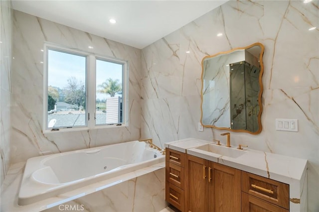 bathroom featuring tiled tub, vanity, and tile walls