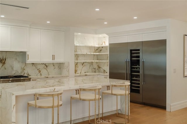 kitchen with white cabinets, a kitchen breakfast bar, light stone counters, and light wood-type flooring