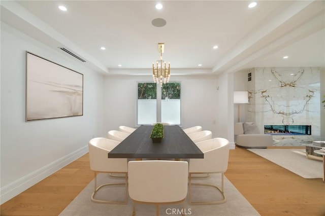 dining space with a raised ceiling, a premium fireplace, light hardwood / wood-style flooring, and a notable chandelier