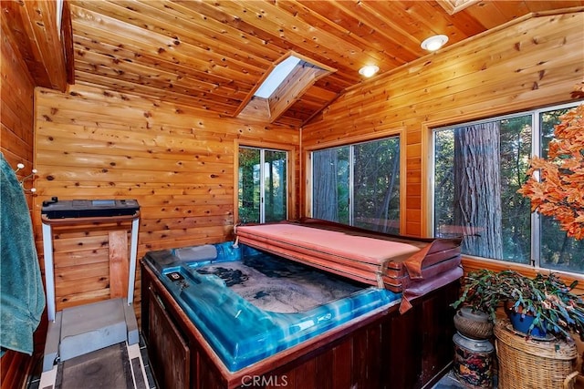 interior space with lofted ceiling with skylight, plenty of natural light, wood walls, and a hot tub