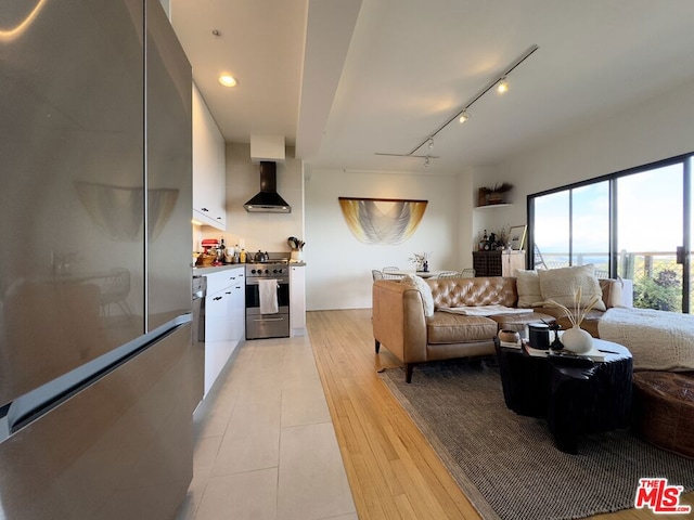 kitchen featuring white cabinetry, wall chimney range hood, light hardwood / wood-style flooring, track lighting, and appliances with stainless steel finishes