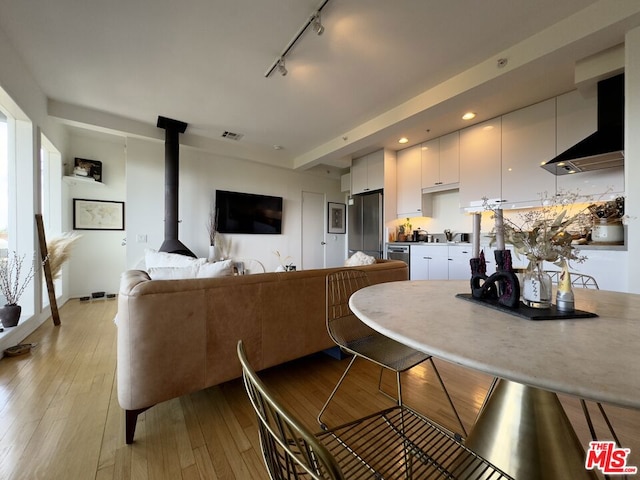 kitchen with a wood stove, white cabinetry, stainless steel fridge, track lighting, and light wood-type flooring