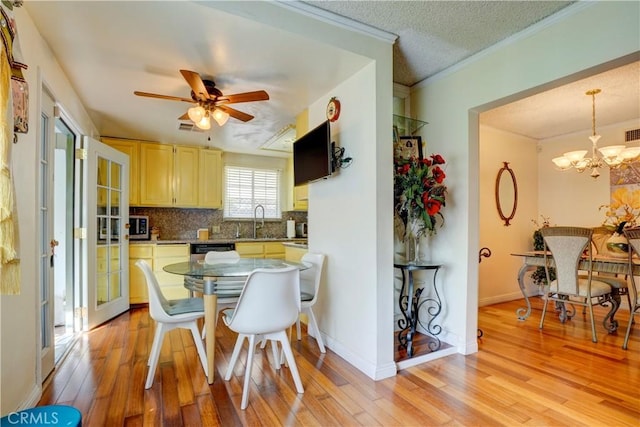 dining space with ceiling fan with notable chandelier, a textured ceiling, light wood-type flooring, and sink