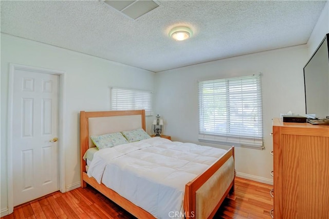 bedroom with baseboards, visible vents, wood finished floors, and a textured ceiling