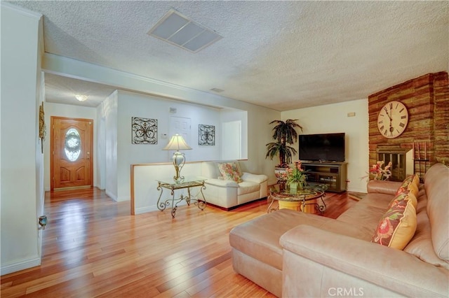 living room featuring a brick fireplace, a textured ceiling, and light hardwood / wood-style flooring