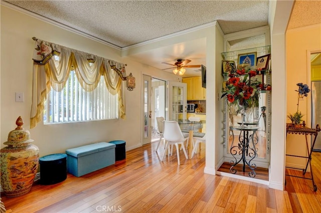 interior space featuring a textured ceiling, a ceiling fan, crown molding, and light wood finished floors