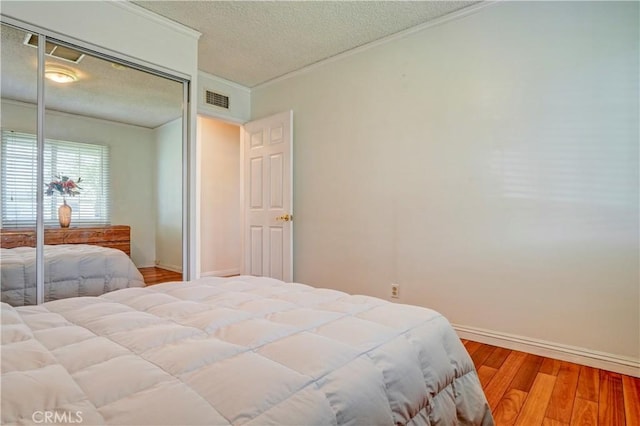 bedroom with a textured ceiling, hardwood / wood-style flooring, a closet, and ornamental molding