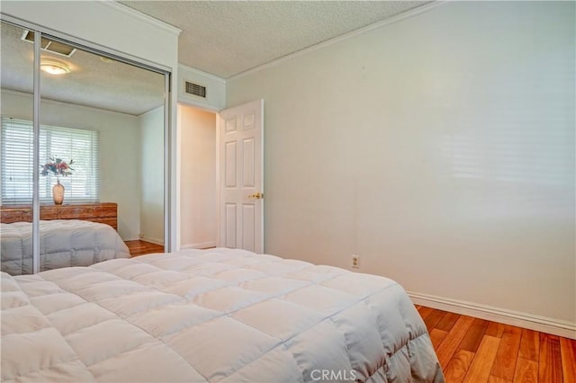 bedroom with ornamental molding, a textured ceiling, visible vents, a closet, and wood finished floors