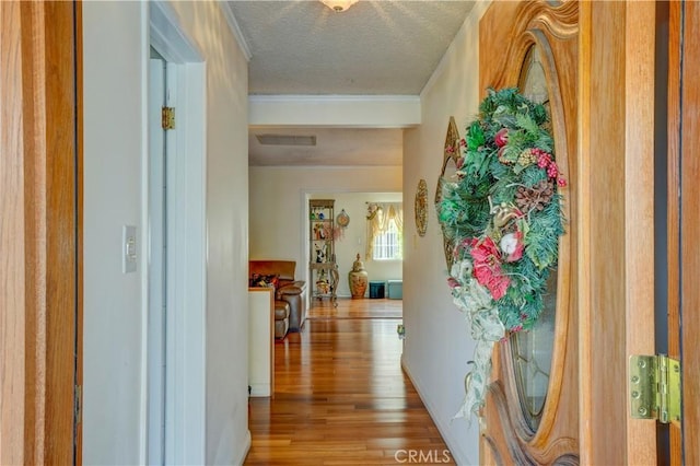 corridor featuring hardwood / wood-style floors, a textured ceiling, and ornamental molding