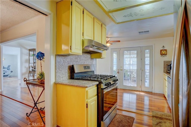 kitchen with light countertops, light wood-type flooring, under cabinet range hood, gas stove, and visible vents