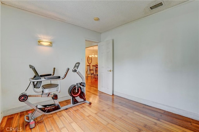 exercise room with wood-type flooring, an inviting chandelier, baseboards, a textured ceiling, and visible vents
