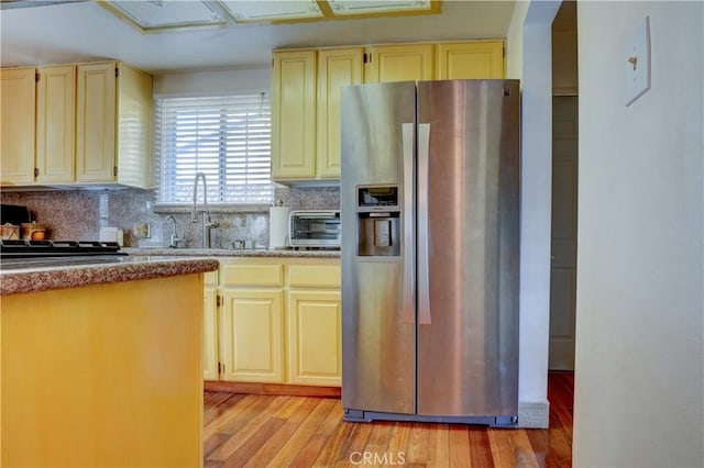 kitchen featuring decorative backsplash, stainless steel fridge, light wood-type flooring, and sink