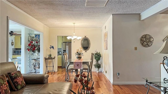 dining space with visible vents, crown molding, light wood-style floors, and an inviting chandelier